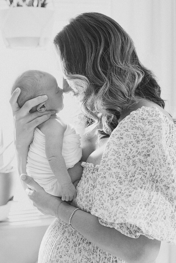 Mom nose-to-nose with baby boy. She's wearing floral-patterned linen dress and has curls in her hair.