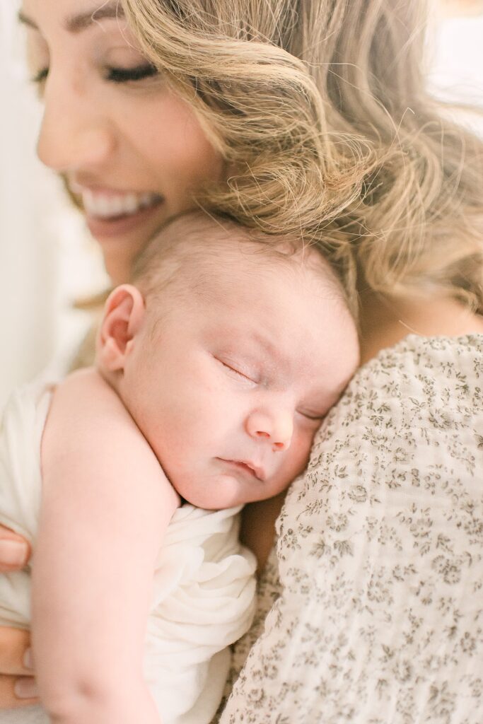 closeup of mom smiling with baby on sleeping on her chest during newborn photography in Gilbert, AZ
