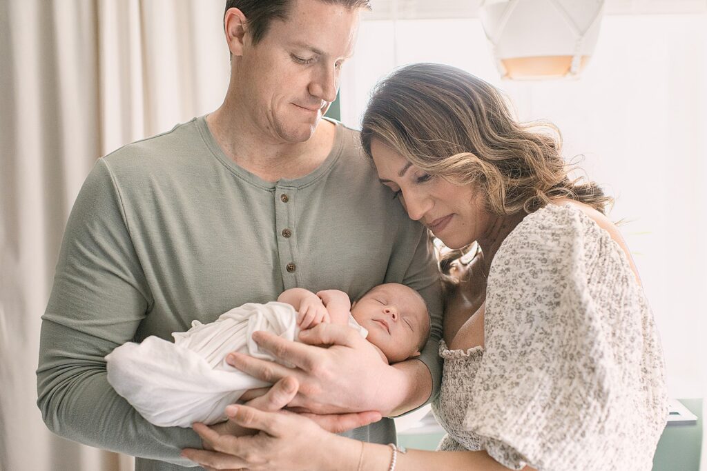 New parents snuggled together and looking at baby boy in dad's arms