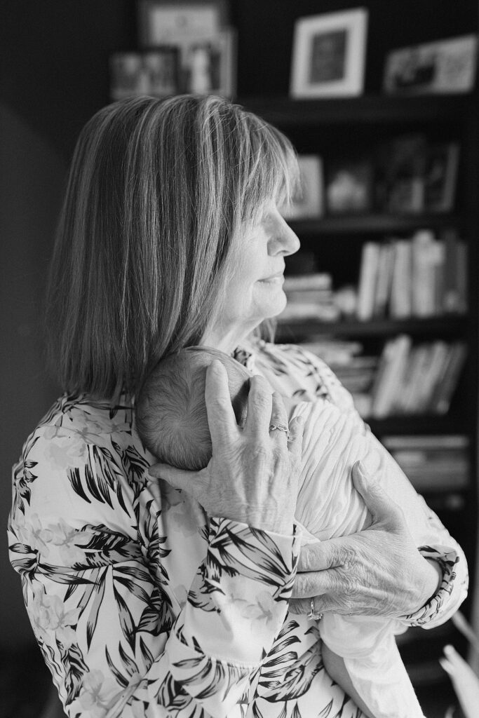 grandmother cradling baby on her chest while she gazes out window