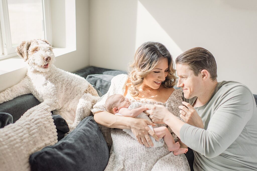 New parents relaxed on couch with dog while holding new baby
