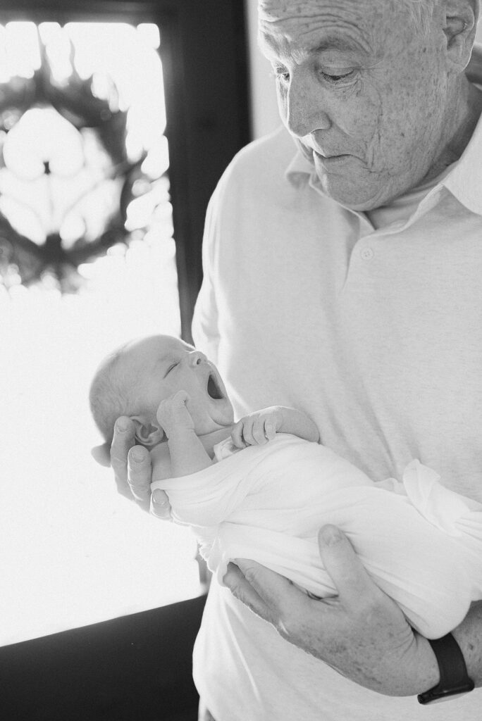 grandfather sweetly admiring yawning baby in his hands. 