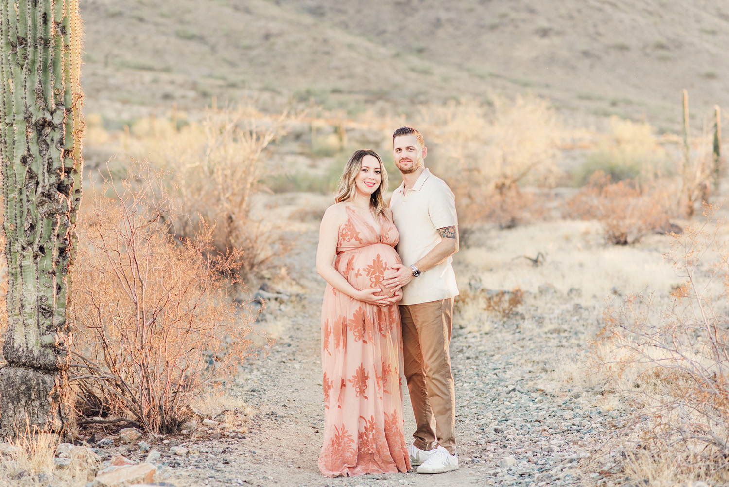 Couple standing with hands on baby bump in desert scenery for phoenix fall family portraits